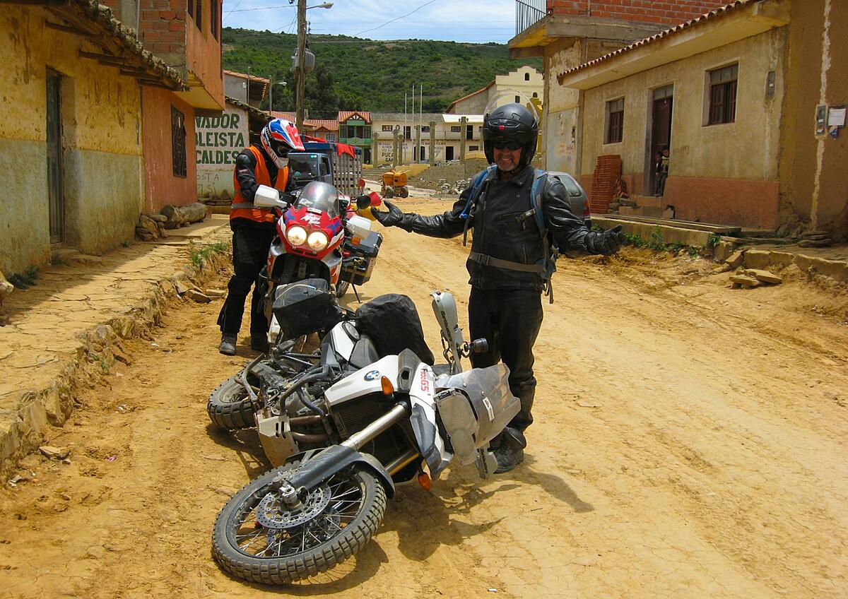Rider dropping his bike on a dirt road through a village in Bolivia.