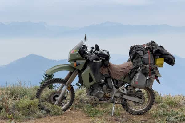 Garrett's KLR 650 sitting along a cliff with mountains in the background with a rackless soft luggage set up.
